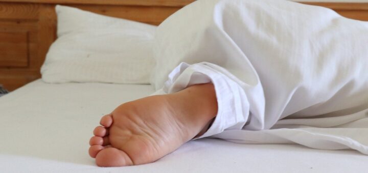 Fuß, der aus der Bettdecke herausragt